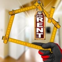 a person holding a house shaped frame with a for rent sign hanging from it