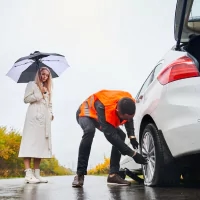 a man and woman fixing a car tire on a rainy day