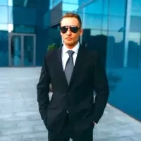 a man in a suit and sunglasses is standing in front of a building