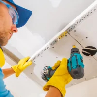 a man in a blue hat and yellow gloves cleaning a white sink