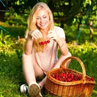 a woman sitting on the grass with a basket of cherries
