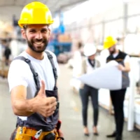 a man in a hard hat and overalls giving a thumbs up