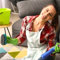 a woman in an apron and green gloves cleaning a living room