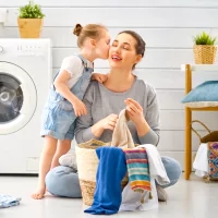 a woman and a child are sitting on the floor in front of a washing machine