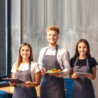 three people in aprons holding plates of food